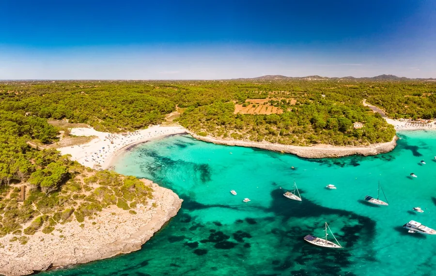 Türkisfarbene Bucht mit Booten und Pinienwald an der Südostküste Mallorcas bei Santanyí, von oben