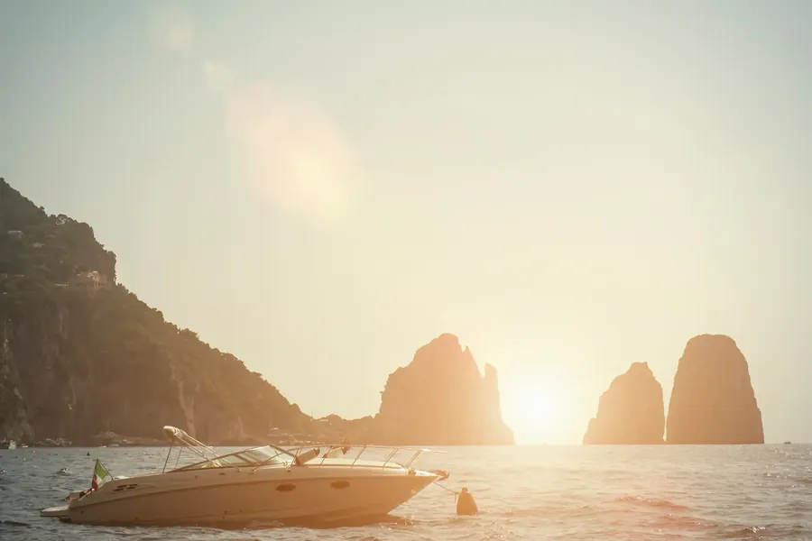 Die Faraglioni-Felsen von Capri bei Sonnenuntergang mit einem vorbeifahrenden Boot