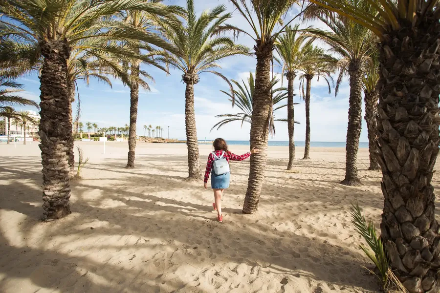 Eine Frau geht an einem breiten Sandstrand entlang, der von Kokospalmen gesäumt ist