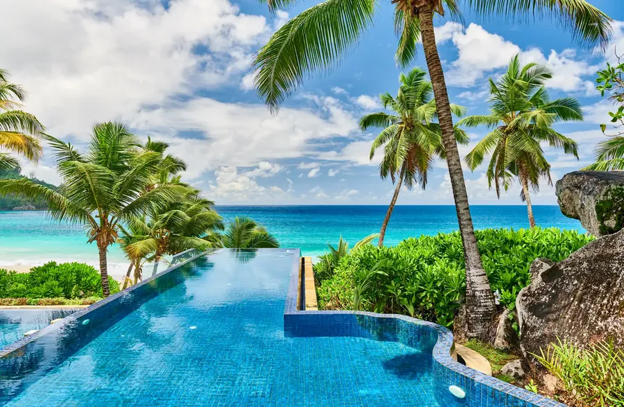 Ein Resortpool unter Palmen neben einem weißen Strand auf den Seychellen