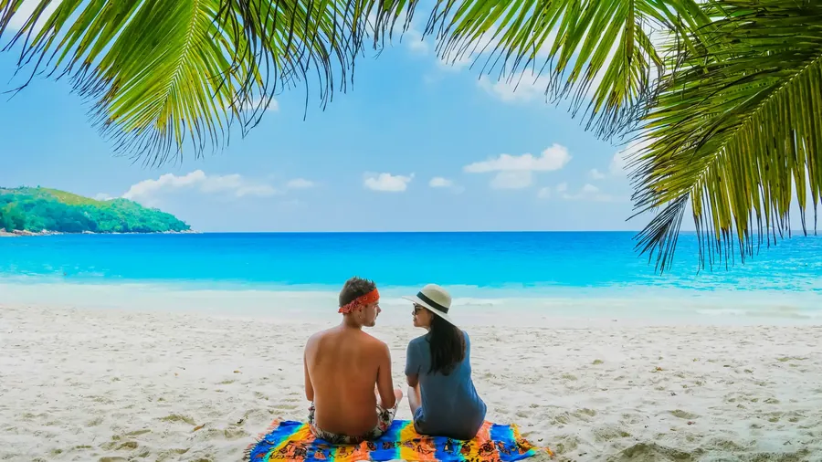 Ein Paar entspannt unter einer geneigten Kokospalme an einem weißen Strand
