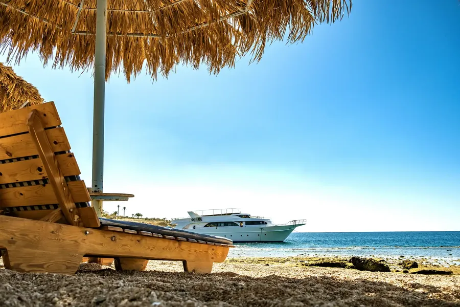 Holzliegen unter einem Strohschirm an einem weißen Strand
