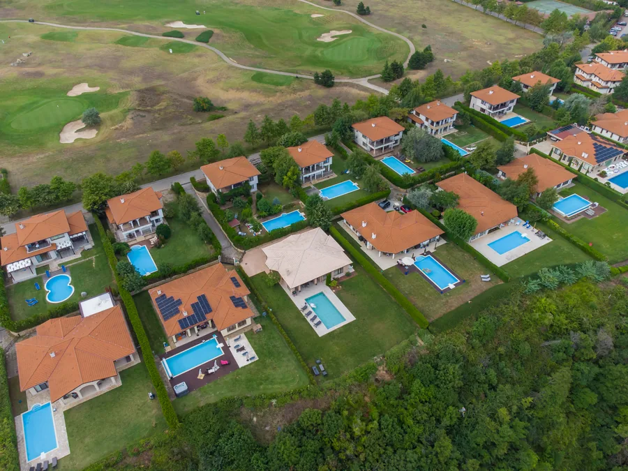 Luftaufnahme von Ferienhäusern mit Ziegeldächern und Pools, gleich daneben die Fairways und Bunker eines Golfplatzes