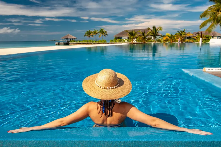 Eine Frau mit Strohhut im Pool mit Blick auf eine Lagune