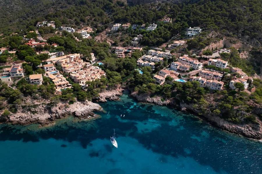 Villen an einem bewaldeten Hang über einer Bucht mit türkisfarbenem Wasser an der Küste Mallorcas, von oben